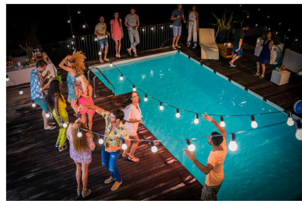 pool party at night; blue pool under a string of lights with people in bathing suits around the deck